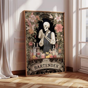May include: A framed print featuring a skeleton bartender mixing a cocktail behind a bar. The artwork is surrounded by floral elements and the words "THE BARTENDER" are displayed on a banner at the bottom. The color palette includes black, gold, and various floral hues.