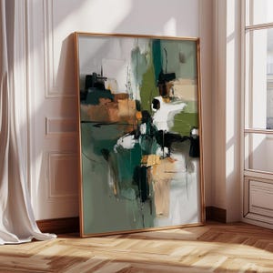 May include: Abstract art print in a gold frame. The artwork features a mix of green, black, white, and tan brushstrokes on a light gray background. The framed art is leaning against a white wall and a wooden floor.