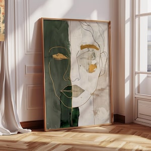 May include: Abstract art print depicting a stylized face. The artwork is split vertically, with one side in dark green and the other in neutral tones. Gold accents highlight the eyes and lips, with gold line art defining the facial features. The artwork is framed in a gold frame.
