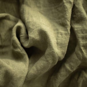 May include: A piece of olive green fabric with a visible woven texture and natural folds. The material displays a matte finish and a consistent earthy tone throughout, characterized by deep creases and soft shadows that highlight the weave.