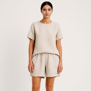 May include: A beige linen short-sleeve top and matching shorts set. The top has a crew neck and a relaxed fit. The shorts are high-waisted with a loose, comfortable design. The outfit is made of a lightweight, breathable fabric, perfect for warm weather.