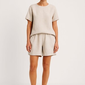 May include: A beige linen two-piece set. The set includes a short-sleeved, crew neck top and matching shorts. The shorts have an elastic waistband. The fabric has a slightly textured appearance.
