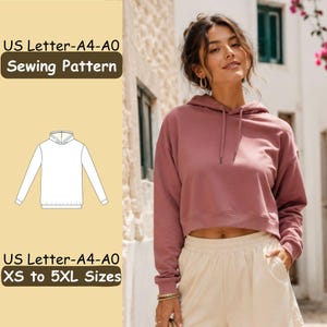 May include: A sewing pattern for a cropped hoodie with long sleeves and a drawstring hood. The text reads US Letter-A4-A0 Sewing Pattern and US Letter-A4-A0 XS to 5XL Sizes. A line drawing of the hoodie is included on a light yellow background.
