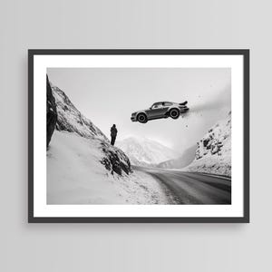 以下が含まれることがあります： 雪山道路の上を飛ぶ銀色のスポーツカーの白黒写真。道路の脇に人が立って、車を上を見ている。