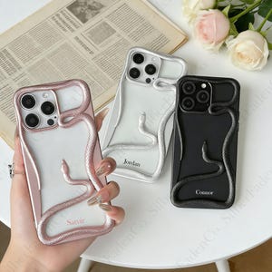 Könnte beinhalten: Drei Handyhüllen mit Schlangenmuster. Eine ist roségoldfarben, eine silberfarben und eine schwarz. Jede Hülle hat eine Schlange, die sich um das Telefon windet. Die Namen "Satvir", "Jordan" und "Connor" sind auf den Hüllen aufgedruckt.