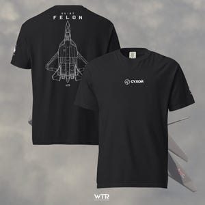 May include: A black short-sleeve t-shirt featuring a white line-art graphic of an SU-57 Felon fighter jet on the back. The front displays a small white circular logo with the Cyrillic text "СУХОЙ". The shirt has a crew neckline and short sleeves.