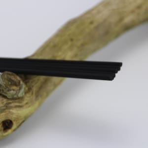 Könnte beinhalten: Ein Satz schwarzer Diffusorstäbchen, die auf einem Stück Treibholz liegen.