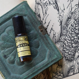 Puede incluir: Un peque&ntilde;o frasco de vidrio marr&oacute;n con un aplicador de bola negro. El frasco est&aacute; etiquetado con "The Scents Old Books" y contiene aceite de salvado de arroz org&aacute;nico y aceites esenciales. La etiqueta tambi&eacute;n indica "Para uso externo &uacute;nicamente - Grado terap&eacute;utico".