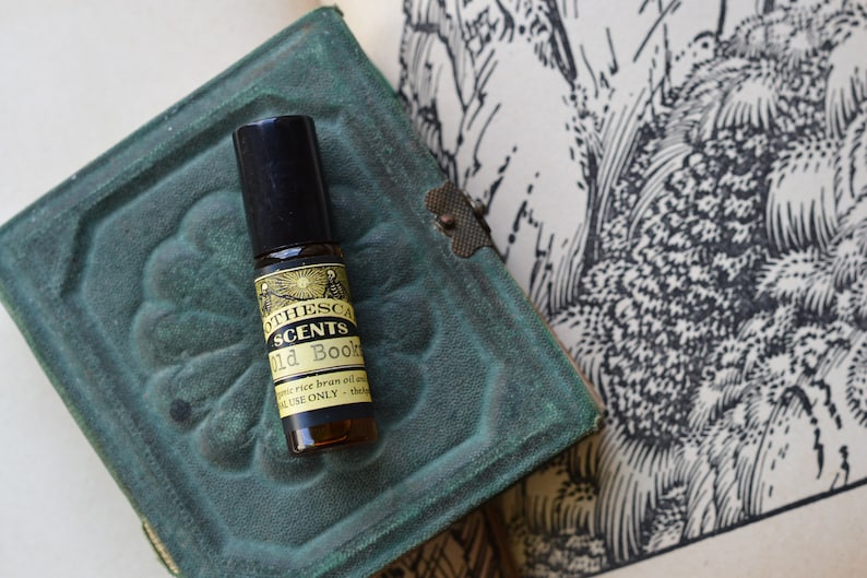 Puede incluir: Un peque&ntilde;o frasco de vidrio marr&oacute;n con un aplicador de bola negro. El frasco est&aacute; etiquetado con "The Scents Old Books" y contiene aceite de salvado de arroz org&aacute;nico y aceites esenciales. La etiqueta tambi&eacute;n indica "Para uso externo &uacute;nicamente - Grado terap&eacute;utico".