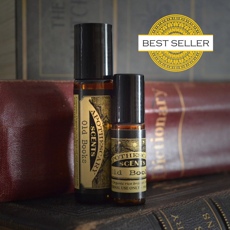 Puede incluir: Dos botellas de vidrio con tapas de rodillo negras y etiquetas que dicen "Apothecary Scents" y "Old Books". Las botellas est&aacute;n sobre una pila de libros antiguos. La imagen tiene una insignia de "Best Seller".