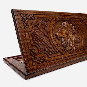 May include: A wooden game board with a lion carved into the lid. The board is closed and the lion's head is facing the right side of the image.