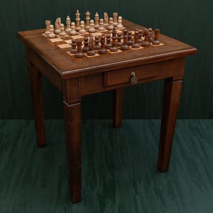 Puede incluir: Mesa de ajedrez de madera marrón con un cajón y un juego de ajedrez completo. La mesa tiene un tablero de ajedrez. Las piezas son de color marrón claro y oscuro. La mesa mide unos 76 cm de altura.