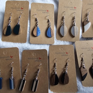 May include: A selection of handmade earrings on brown cards. The earrings combine wood and resin in designs with blue, white, and black. Each card is labelled "Handmade with love."
