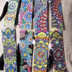 May include: A selection of vibrantly coloured bookmarks, each displaying a detailed mandala pattern. The bookmarks feature a variety of colours, such as blue, pink, yellow, and purple, and are finished with decorative tassels. Small, sparkling embellishments are also present.