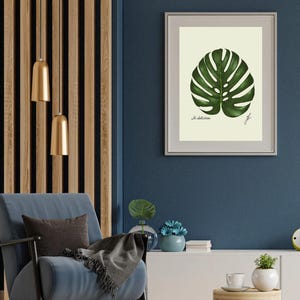 Monstera print in a white frame with passpartout hanging on a blue wall
