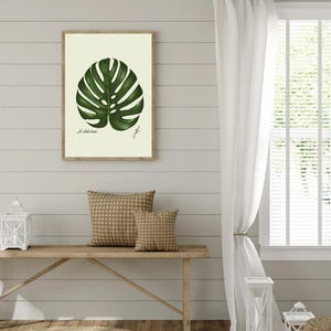 Monstera print hanging on a wooden cabin wall above a bench with two brown pillows