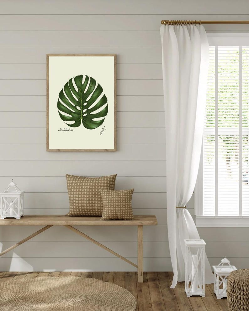 Monstera print hanging on a wooden cabin wall above a bench with two brown pillows