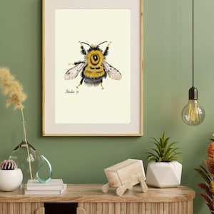 Bumblebee print in a wooden frame with white passpartout hanging on a green wall above the dresser