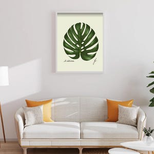 Monstera print in a white framed print on a white wall above a white couch