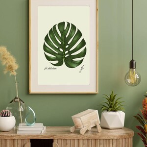 Monstera print in a wooden frame with white passpartout hanging on a green wall above the dresser