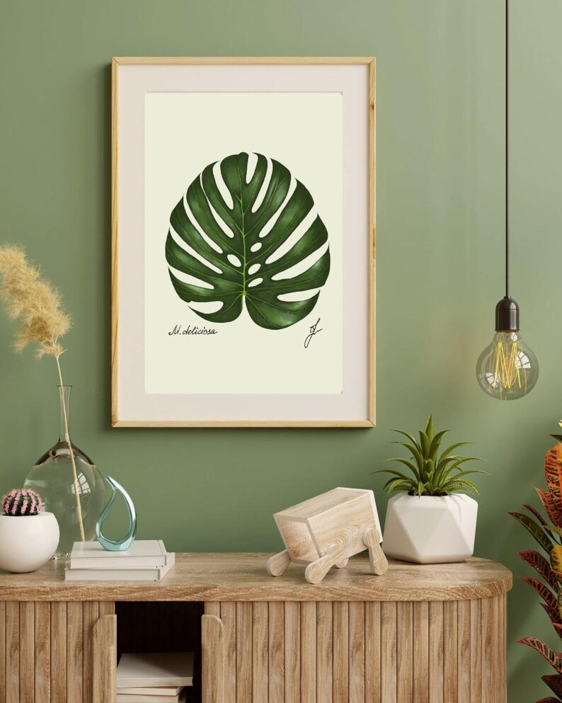 Monstera print in a wooden frame with white passpartout hanging on a green wall above the dresser