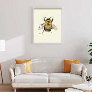 Bumblebee print in a white framed print on a white wall above a white couch