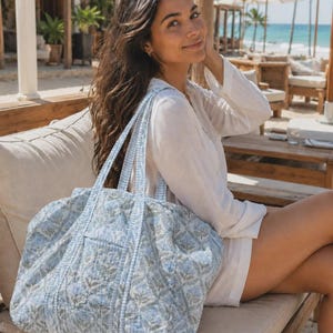 Peut inclure: Un grand sac fourre-tout matelass&eacute; arborant un motif floral imprim&eacute; en bleu clair et blanc. Le sac est dot&eacute; de deux anses assorties en tissu et d'une poche ext&eacute;rieure rectangulaire sur le devant, fabriqu&eacute; en textile piqu&eacute; souple.