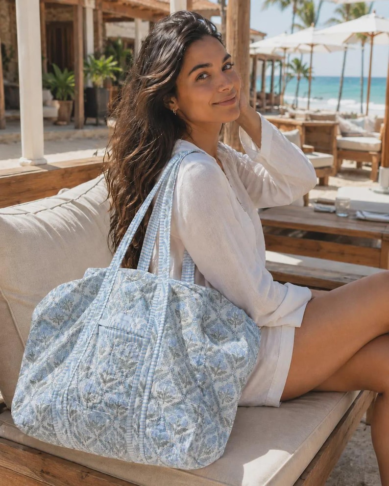 Peut inclure: Un grand sac fourre-tout matelass&eacute; arborant un motif floral imprim&eacute; en bleu clair et blanc. Le sac est dot&eacute; de deux anses assorties en tissu et d'une poche ext&eacute;rieure rectangulaire sur le devant, fabriqu&eacute; en textile piqu&eacute; souple.
