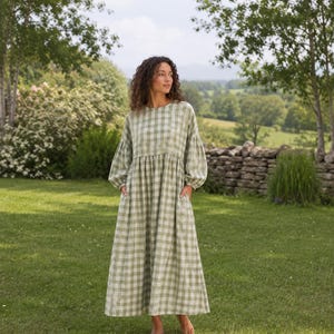 Pode incluir: Um vestido de manga comprida at&eacute; ao tornozelo com um padr&atilde;o de xadrez vichy em verde s&aacute;lvia e branco. A pe&ccedil;a tem um decote redondo, uma cintura franzida, mangas volumosas com punhos ajustados e dois bolsos laterais.
