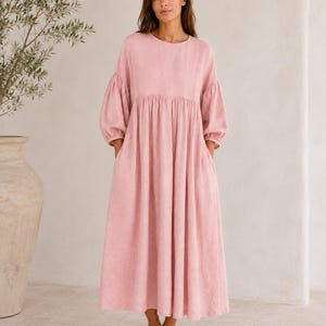 Pode incluir: Um vestido midi em tom rosa seco com decote redondo, mangas compridas volumosas com punhos franzidos e uma saia fluida e descontra&iacute;da com bolsos laterais. A pe&ccedil;a &eacute; confecionada em tecido texturizado e termina a meio da barriga da perna.
