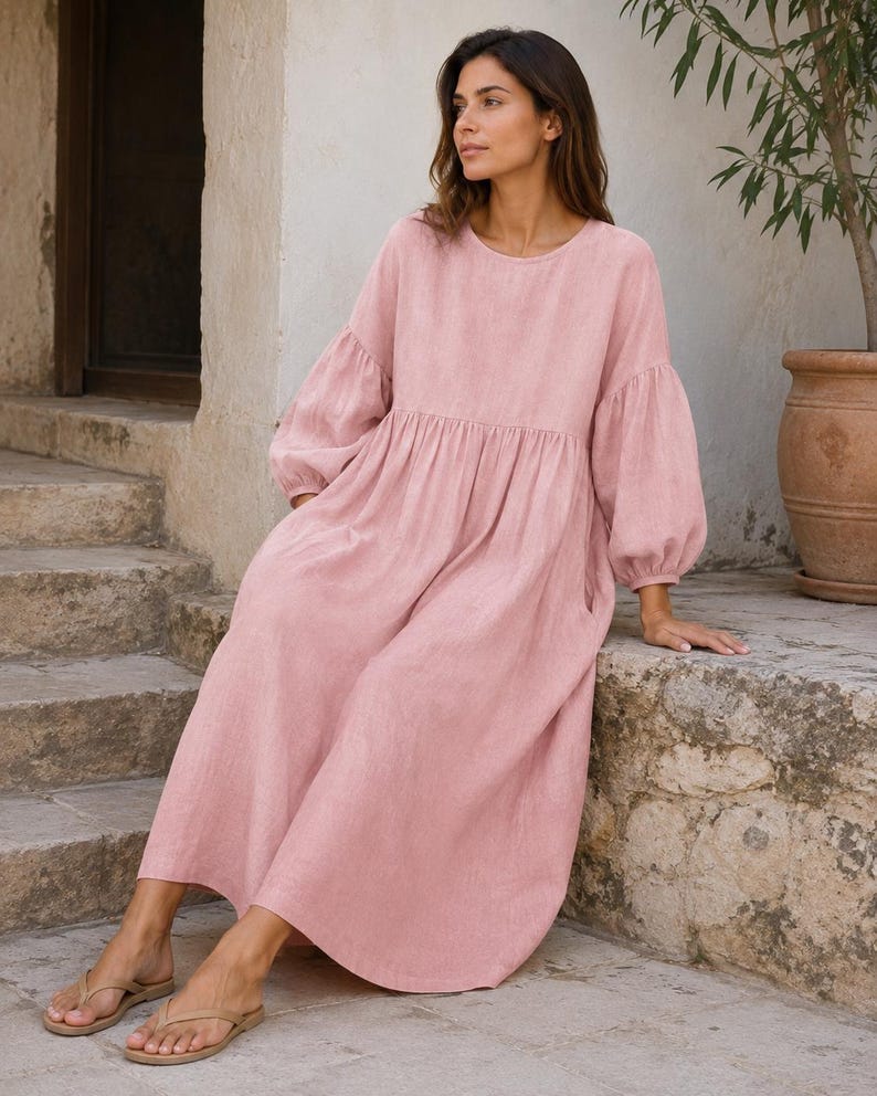 Pode incluir: Um vestido midi em rosa empoeirado com decote redondo, mangas compridas volumosas com punhos franzidos e uma silhueta relaxada e solta que cai at&eacute; ao meio da barriga da perna. A pe&ccedil;a apresenta uma costura franzida na cintura e bolsos.