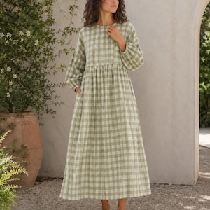 Pode incluir: Um vestido de manga comprida e comprimento at&eacute; ao tornozelo com um padr&atilde;o de xadrez vichy em verde s&aacute;lvia e branco. A pe&ccedil;a apresenta um decote redondo, uma cintura franzida e mangas largas com punhos el&aacute;sticos, criando uma silhueta fluida.