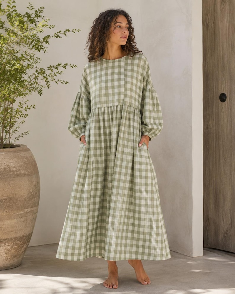 Pode incluir: Um vestido comprido at&eacute; ao ch&atilde;o de manga comprida com um padr&atilde;o de xadrez vichy em verde s&aacute;lvia e branco. A pe&ccedil;a apresenta um decote redondo, uma cintura franzida e mangas largas com punhos el&aacute;sticos, criando uma silhueta solta e fluida.