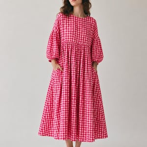 Pode incluir: Um vestido de comprimento midi com um padr&atilde;o vibrante de xadrez vichy em rosa choque e branco. A pe&ccedil;a apresenta um decote redondo, mangas bufantes volumosas de tr&ecirc;s quartos com punhos franzidos e uma saia solta com dois bolsos laterais.