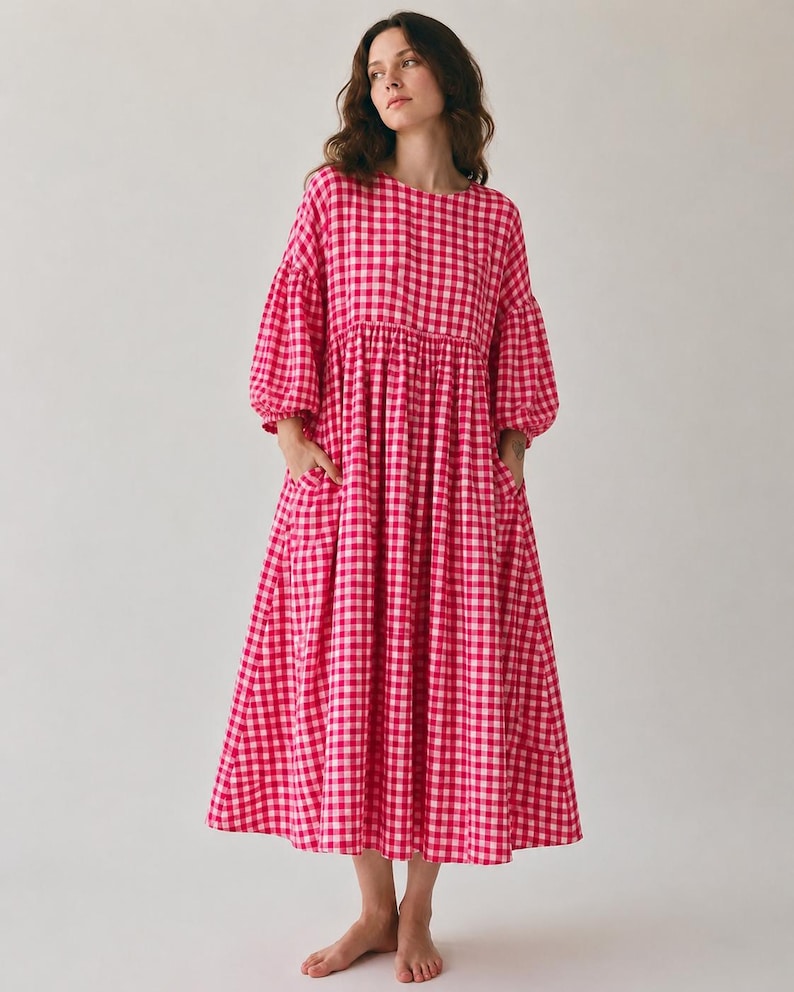 Pode incluir: Um vestido de comprimento midi com um padr&atilde;o vibrante de xadrez vichy em rosa choque e branco. A pe&ccedil;a apresenta um decote redondo, mangas bufantes volumosas de tr&ecirc;s quartos com punhos franzidos e uma saia solta com dois bolsos laterais.