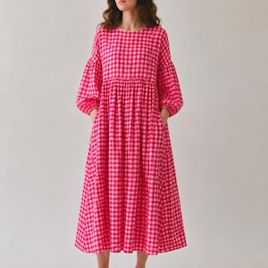 Pode incluir: Um vestido de comprimento midi com um padr&atilde;o vibrante de xadrez vichy em rosa choque e branco. A pe&ccedil;a apresenta um decote redondo, mangas compridas volumosas com punhos franzidos, cintura marcada e uma saia ampla e fluida com bolsos laterais.