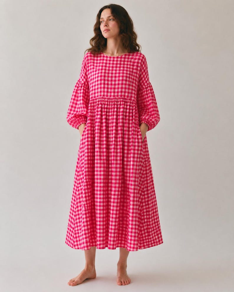 Pode incluir: Um vestido de comprimento midi com um padr&atilde;o vibrante de xadrez vichy em rosa choque e branco. A pe&ccedil;a apresenta um decote redondo, mangas compridas volumosas com punhos franzidos, cintura marcada e uma saia ampla e fluida com bolsos laterais.