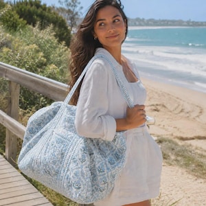 Peut inclure: Un grand sac fourre-tout matelass&eacute; arborant un motif floral bleu clair et blanc. Le sac est dot&eacute; de deux bandouli&egrave;res et d'une base rectangulaire, fabriqu&eacute; avec une texture en tissu piqu&eacute; pr&eacute;sentant un motif botanique r&eacute;p&eacute;titif sur l'ensemble.