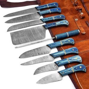 May include: A collection of eight kitchen knives with blue wooden handles and patterned steel blades. The knives are displayed on a brown leather roll. The set includes different knife types, including a chef's knife, a bread knife, and a cleaver.
