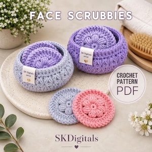 May include: Two round, crocheted baskets in light blue and purple, each containing matching circular face scrubbies with a floral texture. A separate light blue and a pink scrubby lie in front. Each basket features a white tag labeled SK Digitals.