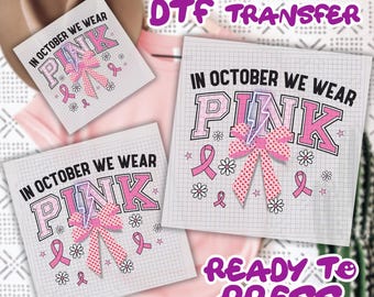May include: DTF transfer sheets with the text "IN OCTOBER WE WEAR PINK" in pink and black. The design includes a pink ribbon, flowers, and pink ribbons. The words "READY TO PRESS" are also visible.