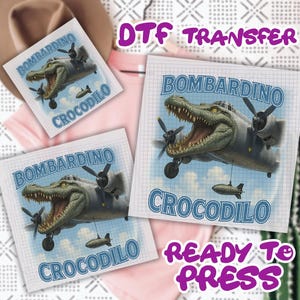 May include: DTF transfer sheets featuring a cartoon alligator in a bomber plane. The text "BOMBARDINO CROCODILO" is displayed in blue, with "READY TO PRESS" in purple. The background is a grid pattern.
