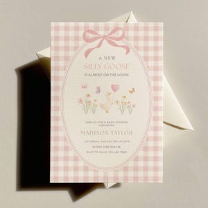 Puede incluir: Una invitación para baby shower con un fondo de cuadros vichy rosa y un marco ovalado decorativo. La invitación presenta un diseño caprichoso con un ganso, flores, mariposas y el texto "A New Silly Goose is Almost on the Loose."