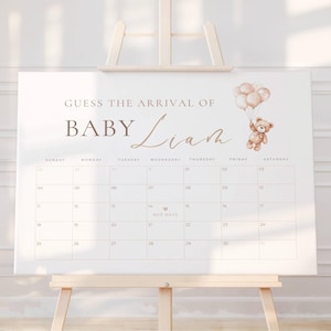 Może przedstawiać: Biały płócienny znak na sztaludze z napisem "GUESS THE ARRIVAL OF BABY Liam". Miś trzymający balony znajduje się po prawej stronie. Poniżej znajduje się siatka kalendarza z datami i dniami tygodnia.