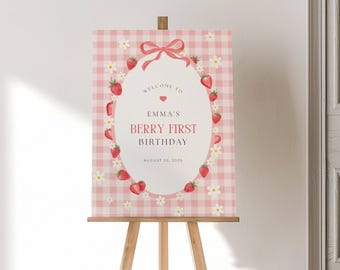 May include: A pink and white gingham welcome sign on a wooden easel. The sign reads "Welcome to Emma's Berry First Birthday" with a strawberry and daisy border. The date "August 20, 2025" is also displayed.