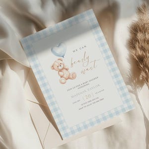 May include: Baby shower invitation with a light blue gingham border. The invitation features a watercolour illustration of a teddy bear holding a heart-shaped balloon. Text reads "We can bearly wait" and event details.