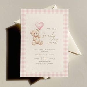 Può includere: Invito per baby shower con bordo a quadretti rosa. L'invito presenta un'illustrazione ad acquerello di un orsacchiotto che tiene in mano un palloncino a forma di cuore. Il testo recita "We can bearly wait" e i dettagli dell'evento.