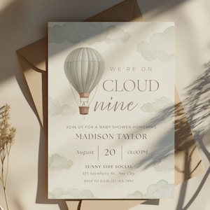 Puede incluir: Una invitación para baby shower con un globo aerostático en acuarela en tonos grises y marrones. El texto dice "We're on Cloud Nine" e incluye detalles para el baby shower de Madison Taylor el 20 de agosto a la 1:00 PM.