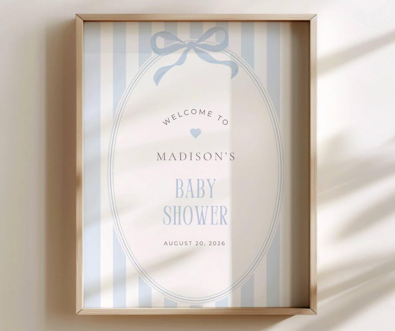 May include: A framed baby shower sign with a light blue and white striped background. The sign features an oval design with the words "Welcome to Madison's Baby Shower" and the date August 20, 2026, in light blue lettering.