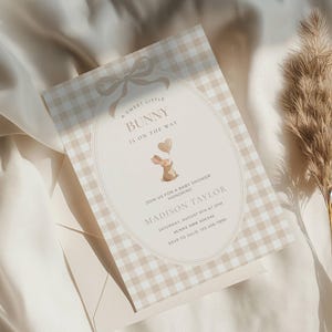 May include: A baby shower invitation with a gingham pattern in beige and white. The invitation features the text "A Sweet Little Bunny Is On The Way" and includes a cartoon bunny holding heart-shaped balloons. The invitation is for Madison Taylor.